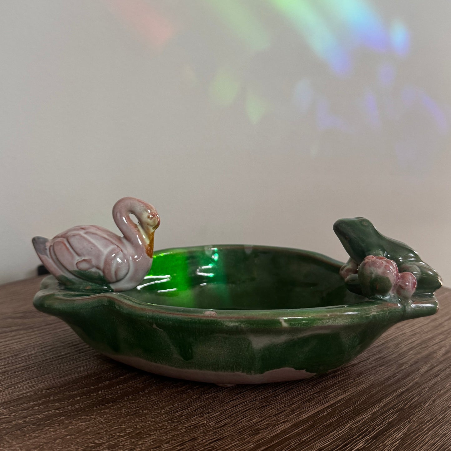 Green ceramic dish with animal figures on a wooden surface, rainbow light effect in the background.